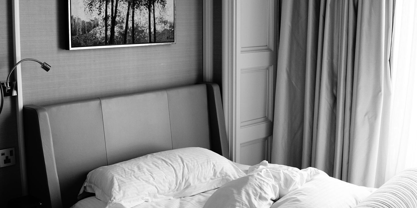 Lugnt hotellrum med bäddad säng, tjocka gardiner och stoppad sänggavel
