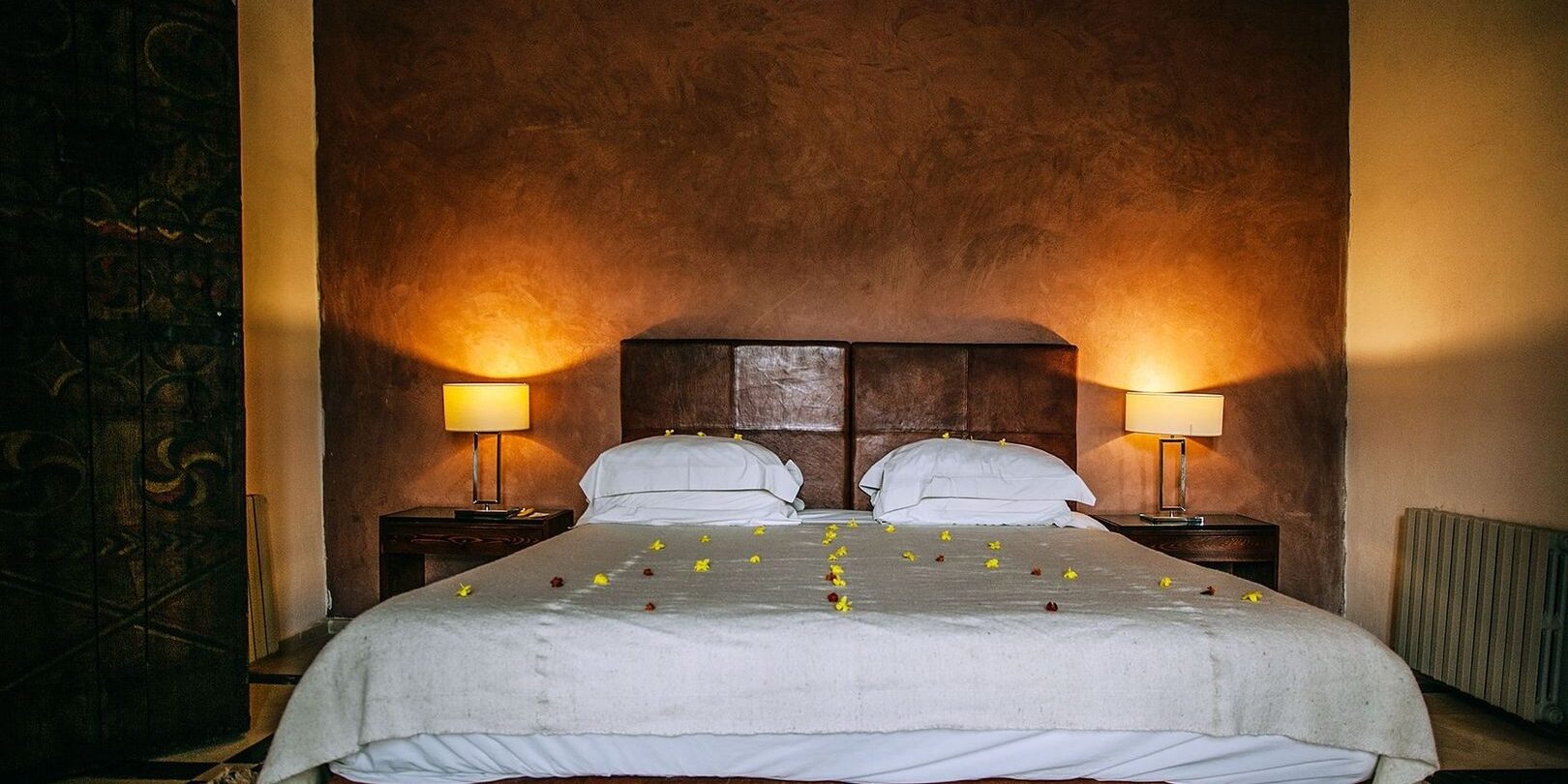 Romantiskt hotellrum med bäddad säng, blommor och varm belysning