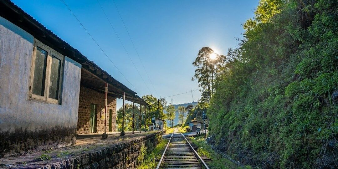 Historisk järnvägsstation med räls och grönskande berg i bakgrunden