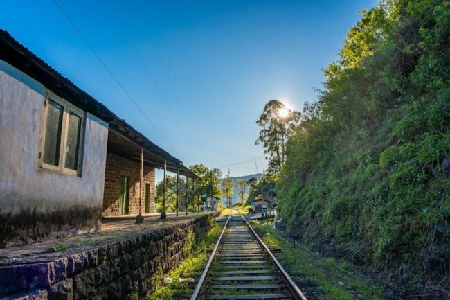 Historisk järnvägsstation med räls och grönskande berg i bakgrunden