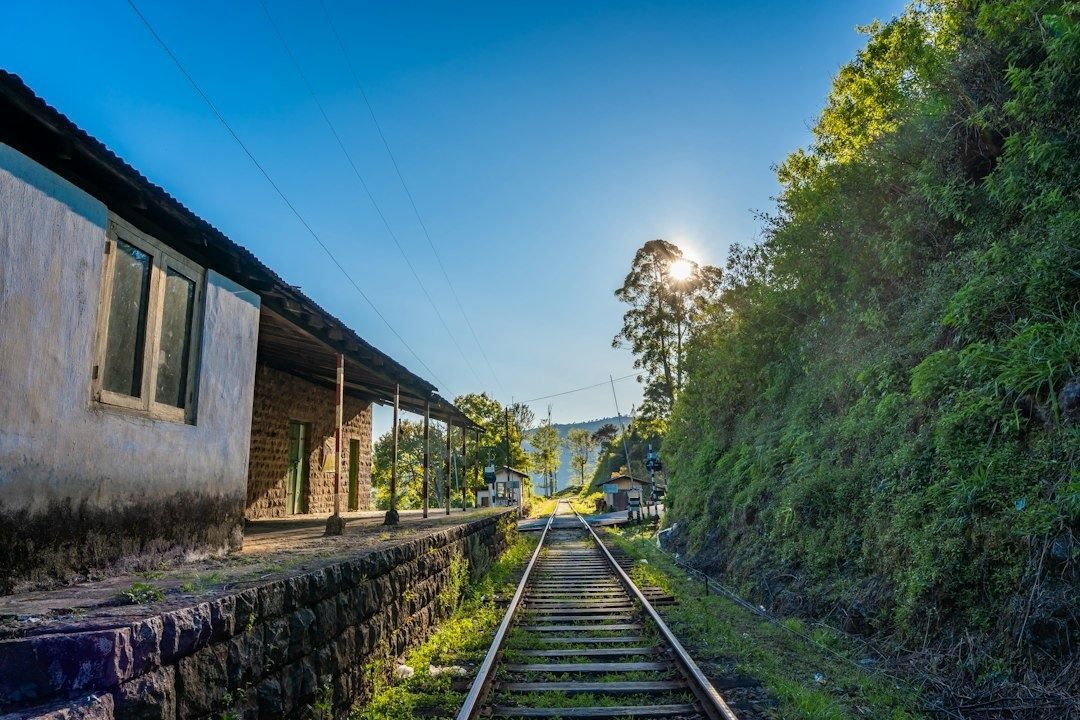 Historisk järnvägsstation med räls och grönskande berg i bakgrunden